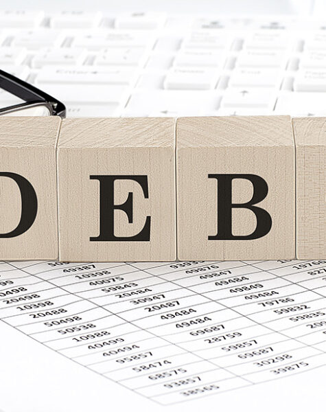 DEBT written on a wooden cube with keyboard , calculator, chart,glasses.Business concept